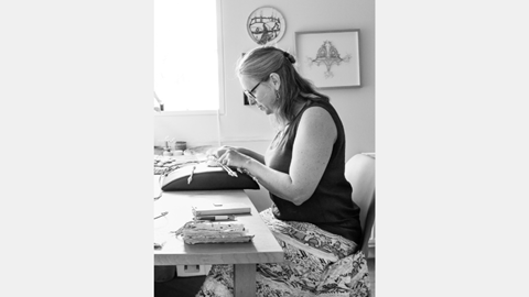 Image shows contemporary bobbin lace artist and maker-in-residence Lindy de Wijn working on an artwork at her desk
