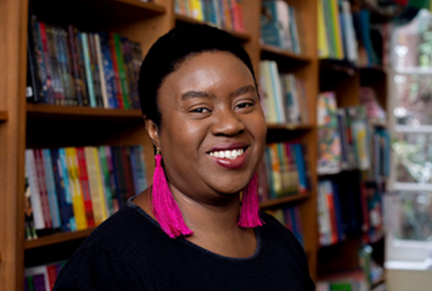 Author Maxine Beneba Clarke smiling in front of a bookshelf filled with books