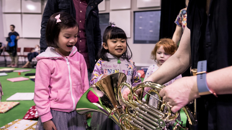 Image shows a group of children at Musical Stories looking at a brass instrument