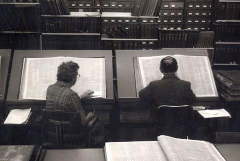 Archival black and white image of two people looking at newspapers from the Library collection