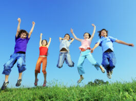 Group of five happy children jumping outdoors